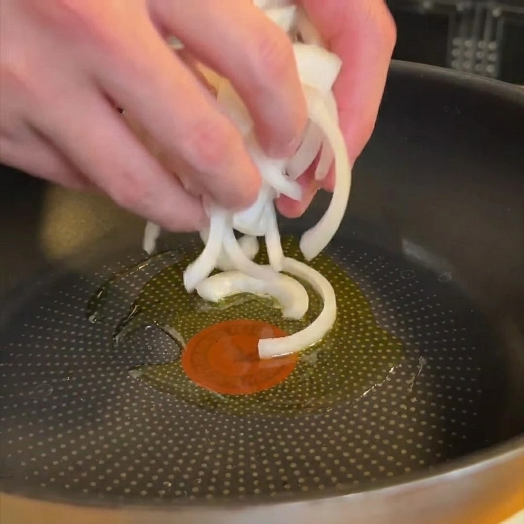 Oignons émincés ramollissant dans une poêle avec de lhuile dolive scintillante.