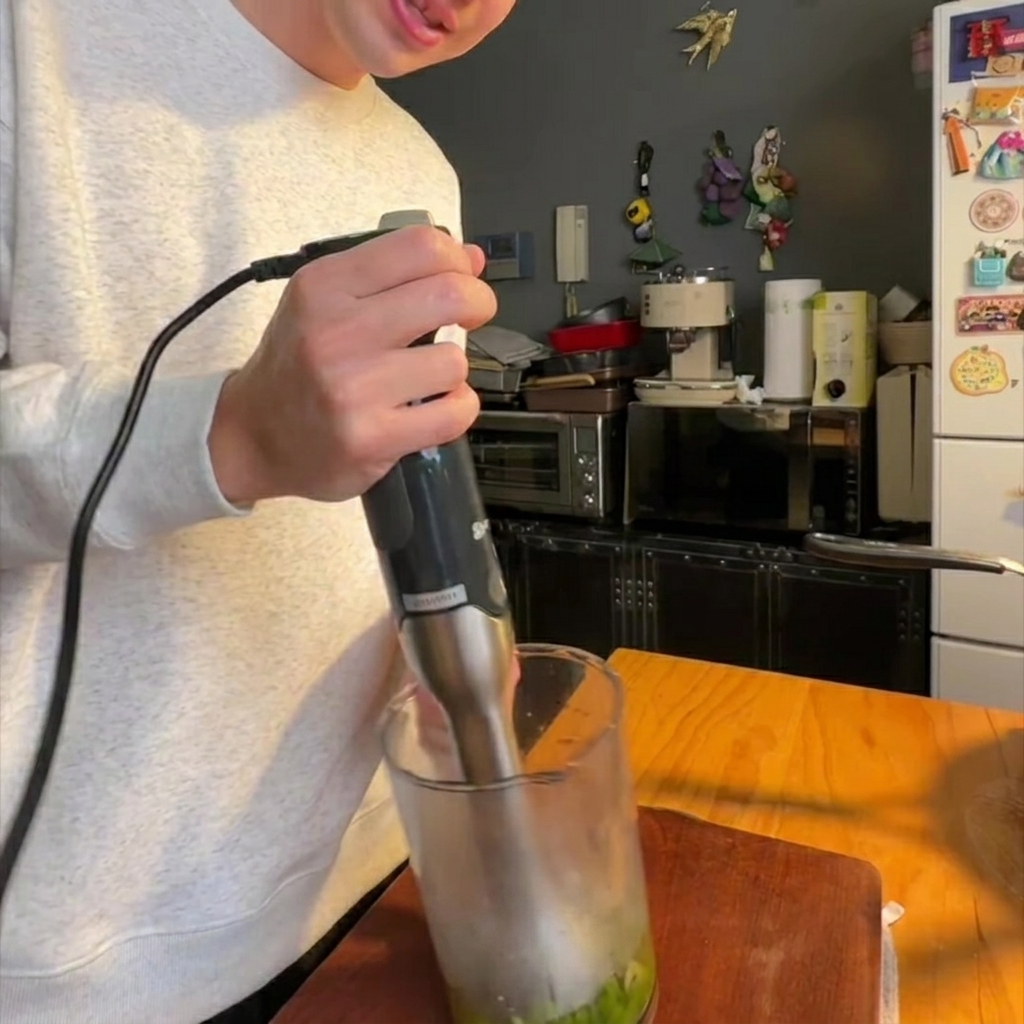 Un mixeur plongeant réduisant les asperges et les oignons cuits en purée lisse dans un récipient.