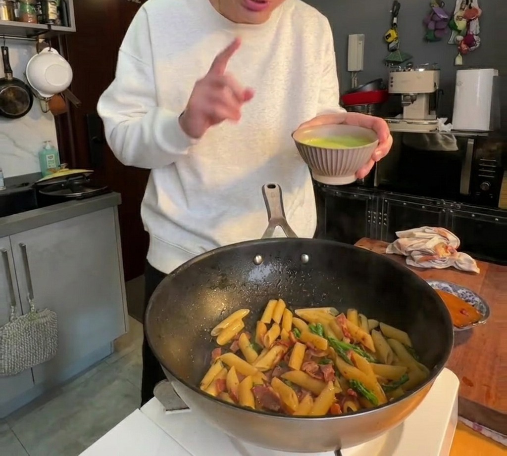 Sauce verte onctueuse versée sur les pennes dans la poêle et mélangée pour enrober.