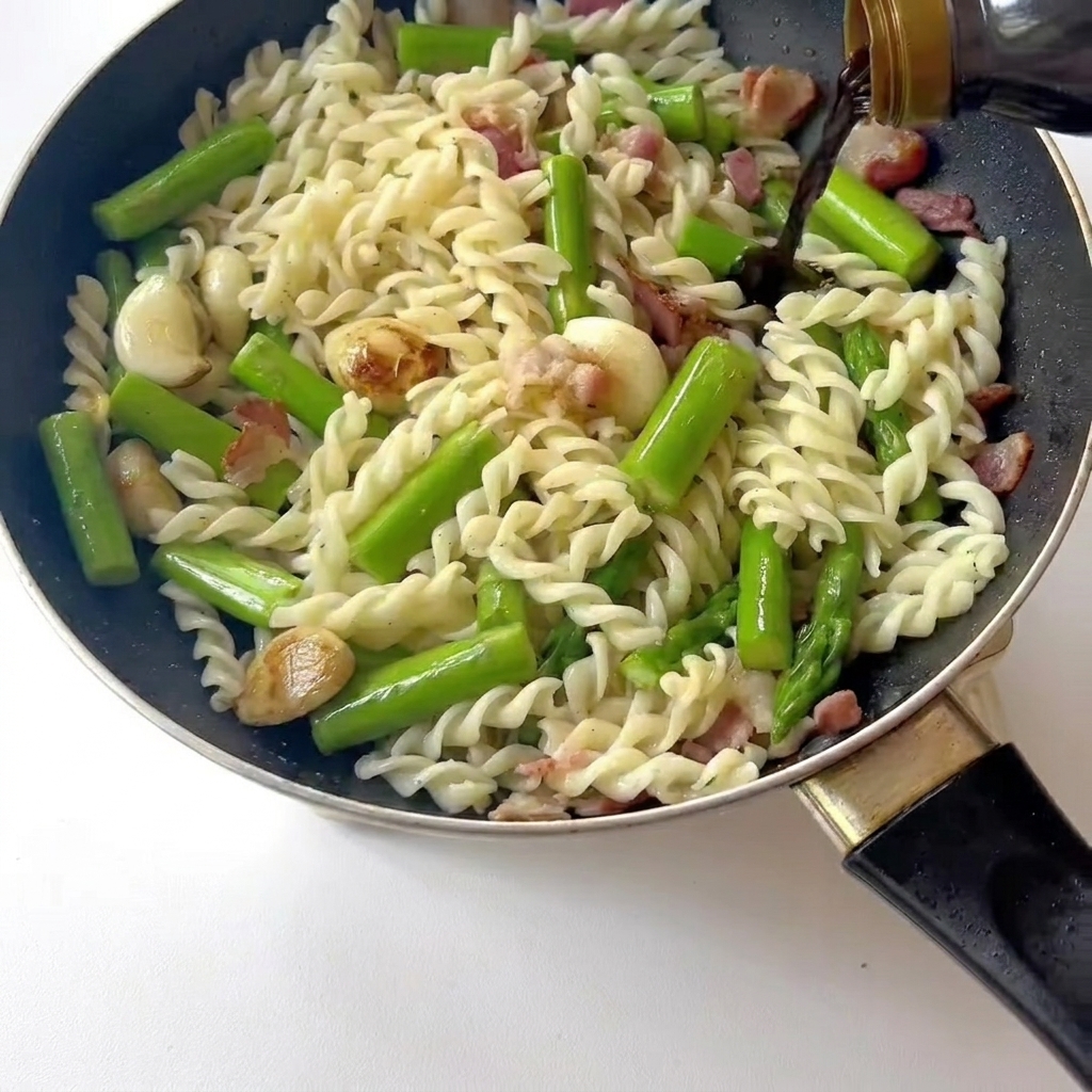 Gros plan dune spatule remuant les pâtes, le bacon et les asperges pendant que la sauce soja est versée.