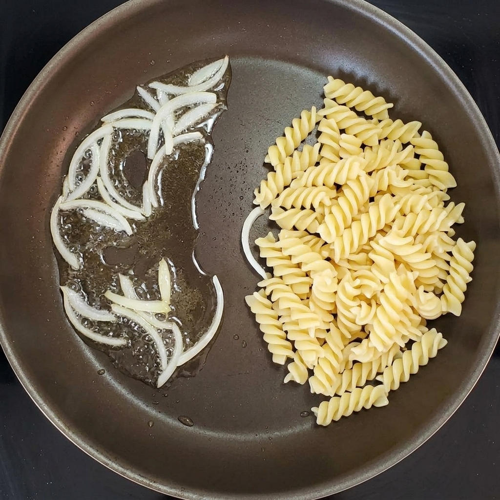 Pâtes spirales mélangées avec des oignons sautés dans une poêle.
