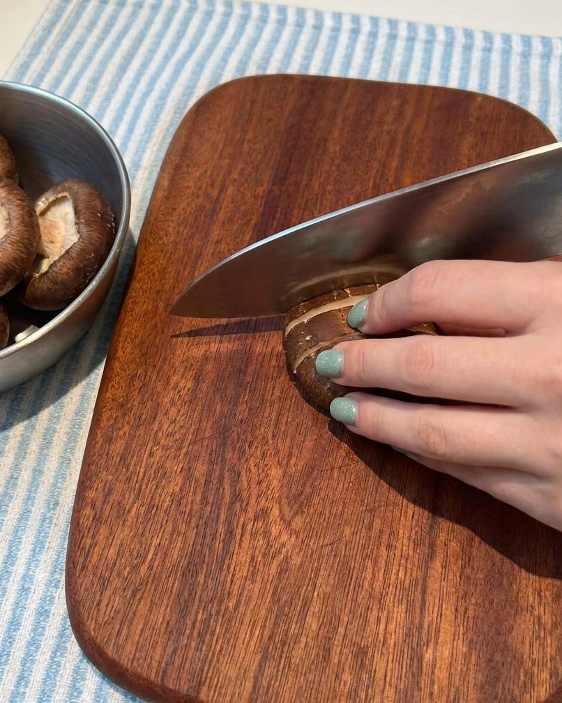 Champignons frais soigneusement coupés en fines lamelles sur une planche à découper en bois.