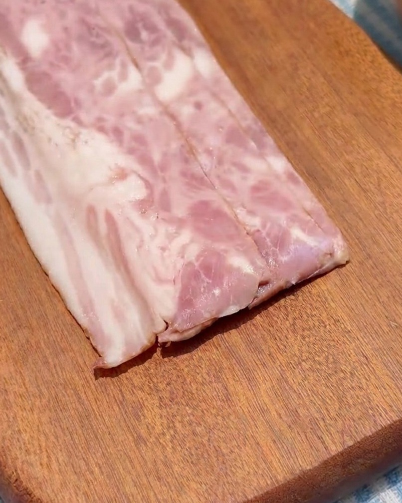 Tranches de bacon coupées en petits carrés réguliers sur une planche à découper en bois.