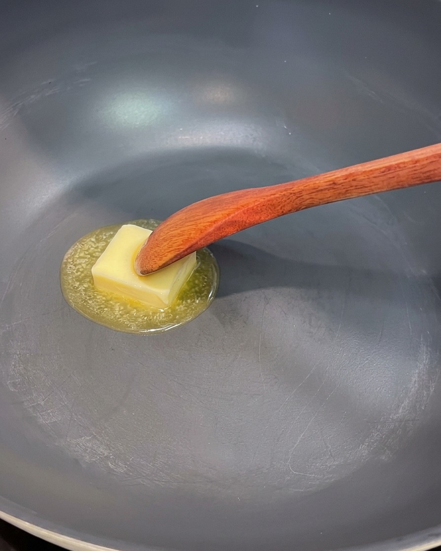 Une poêle avec du beurre fondant, des oignons rouges, des champignons et des morceaux dasperges en cours de cuisson.