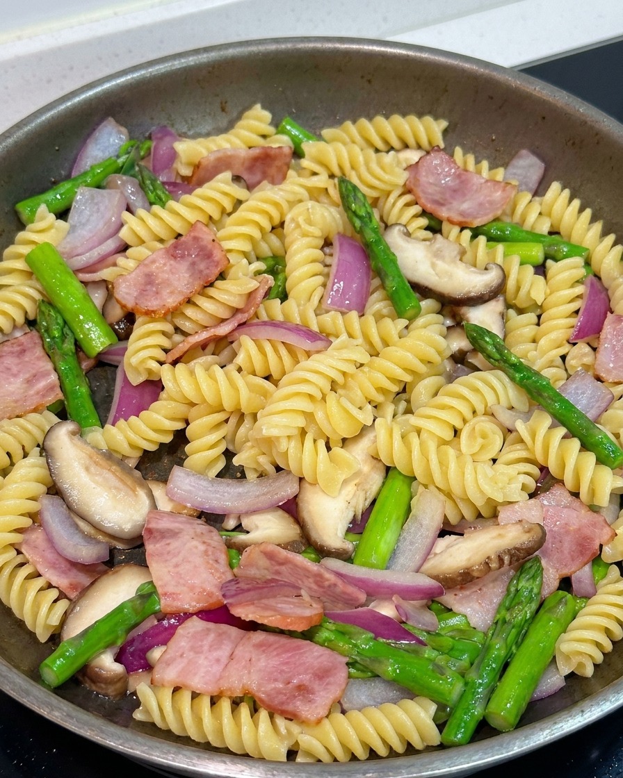 Pâtes mélangées avec les légumes et le bacon dans une poêle, assaisonnées avec du poivre noir et de la sauce soja.