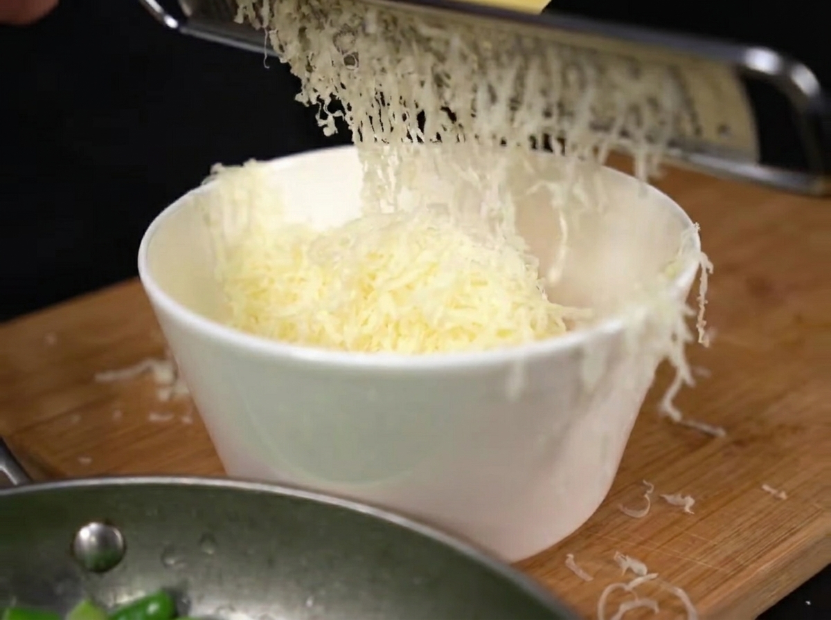 Du parmesan fraîchement râpé tombant en monticule sur les jaunes dœufs dans un bol.