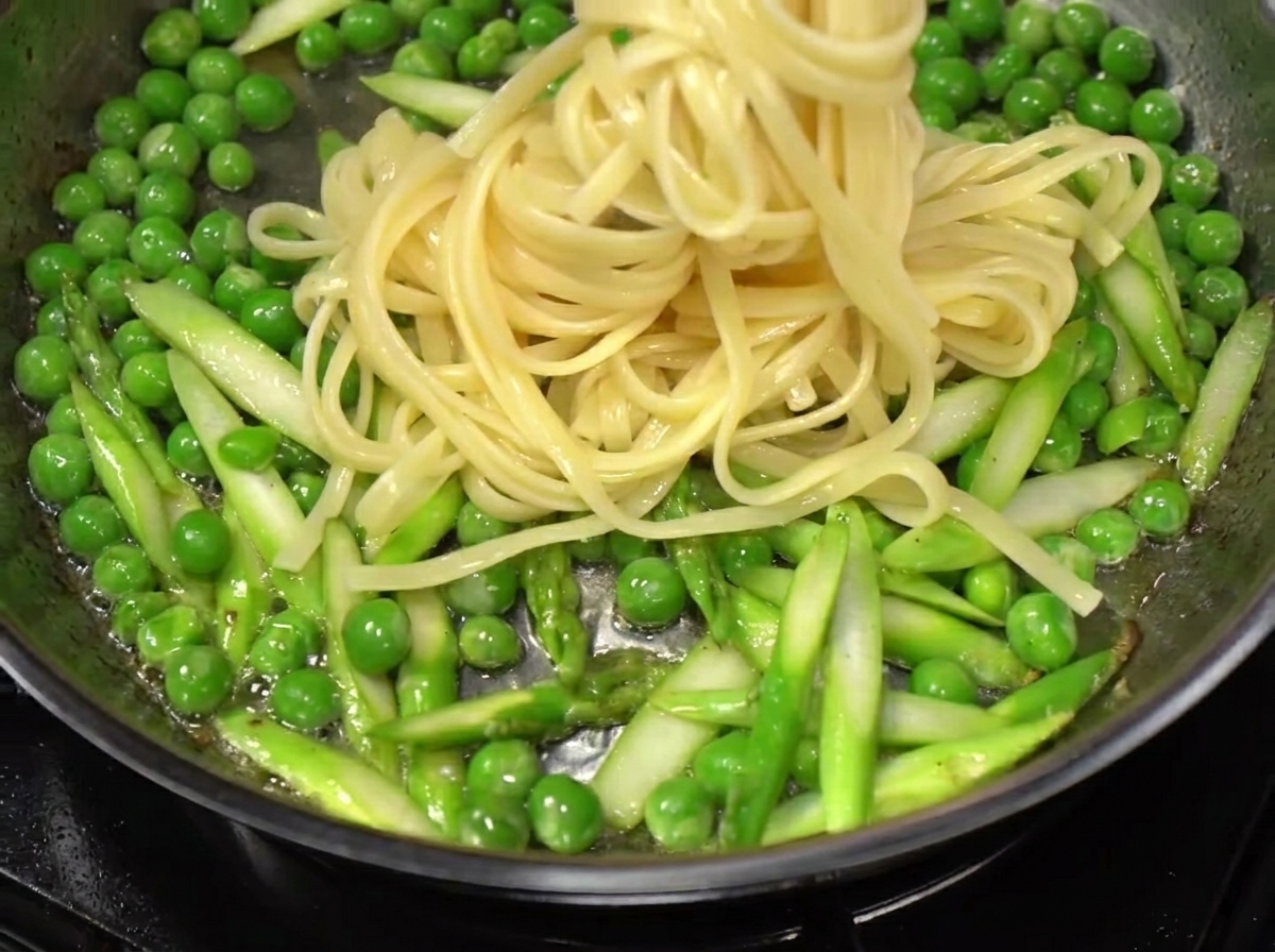 Spaghettis égouttés ajoutés dans une poêle avec les légumes et le bacon.
