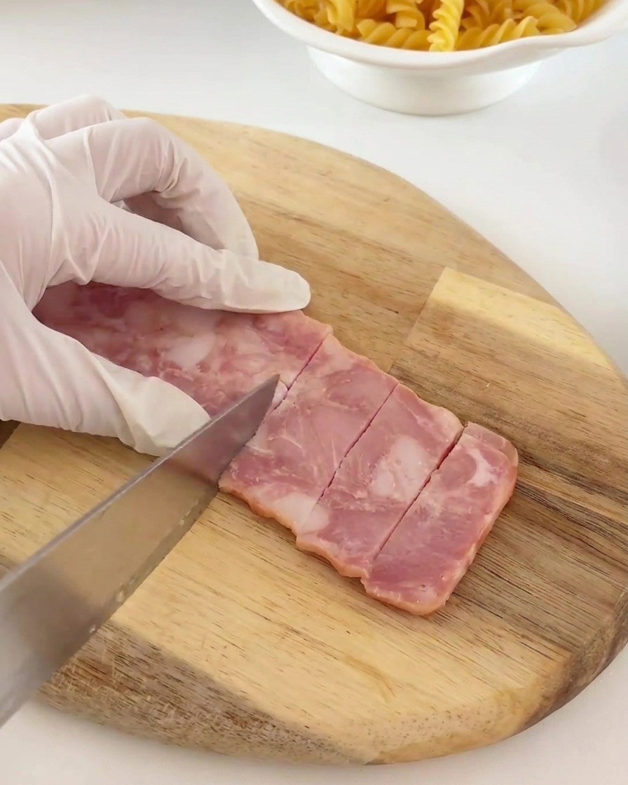 Tranches de bacon coupées en petits morceaux rectangulaires réguliers sur une planche.
