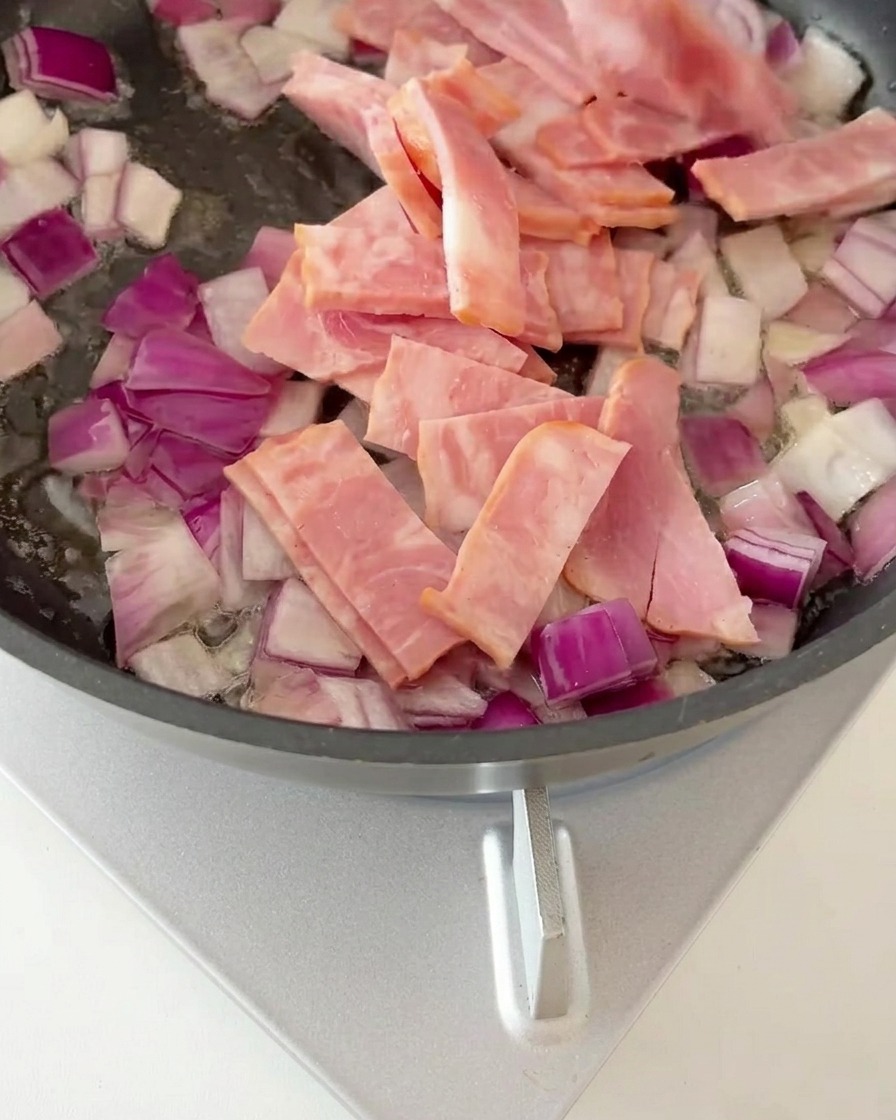 Morceaux de bacon mélangés aux oignons sautés dans une poêle, commençant à dorer.