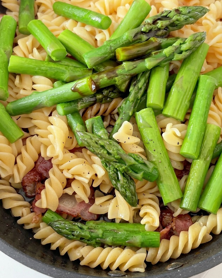 Poêle contenant des fusilli cuits, des asperges vertes et du bacon, en cours dassaisonnement.