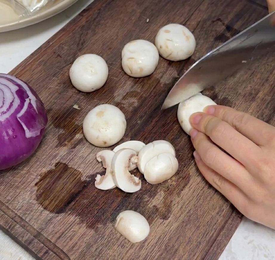 Champignons de Paris frais coupés en fines tranches uniformes sur une planche à découper en bois.