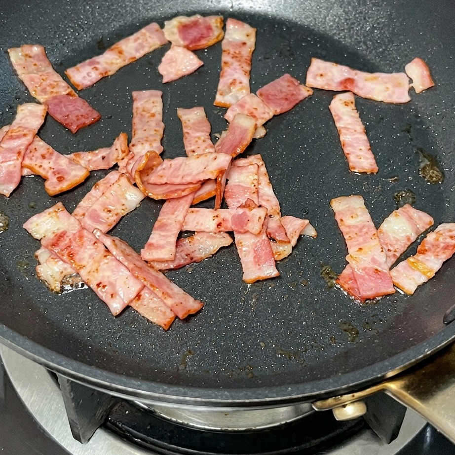 Une noisette de beurre fondant dans la poêle avec les morceaux de bacon grillés.