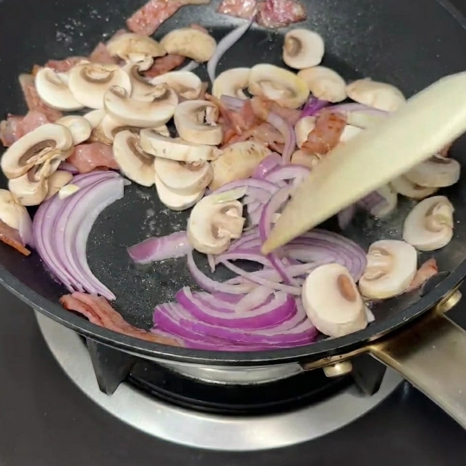Oignons rouges émincés et champignons sautant dans la poêle avec le bacon.