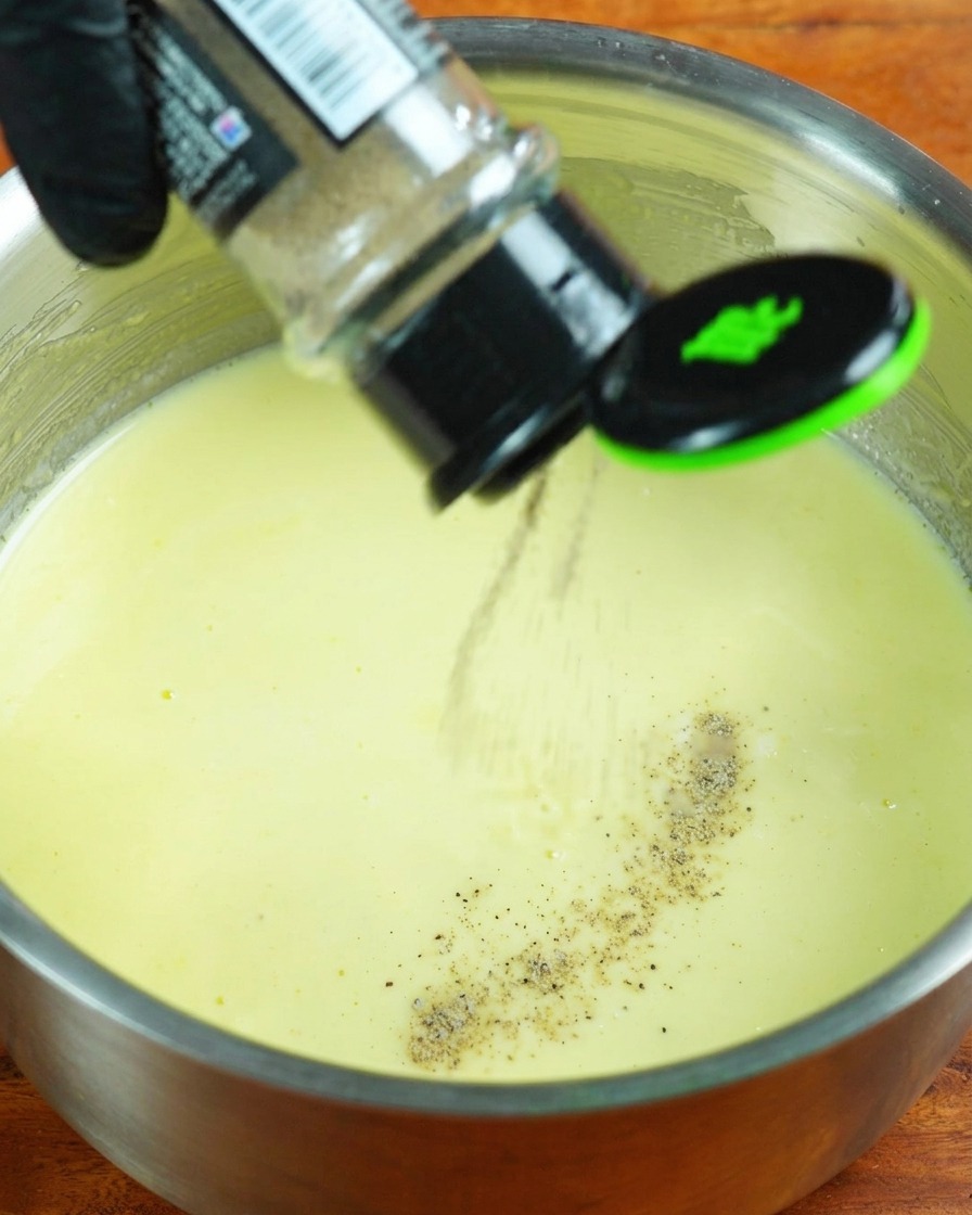 Crème liquide, poivre blanc et sel ajoutés à la sauce au lait frémissante.