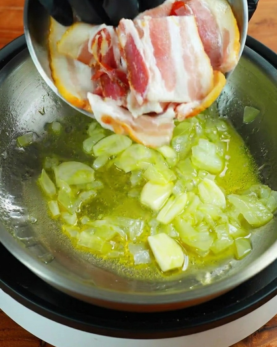 Trois tranches de bacon cru ajoutées dans une poêle contenant lail et loignon sautés.