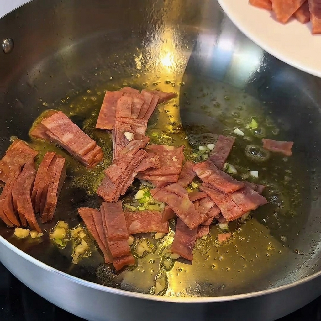 Morceaux dail et de bacon sautés dans du beurre fondu dans une poêle en métal.