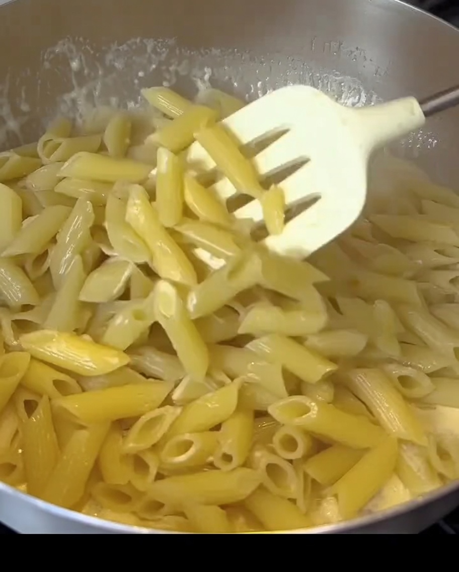 Pennes mélangées dans une sauce blanche crémeuse avec des morceaux de bacon dans une poêle.