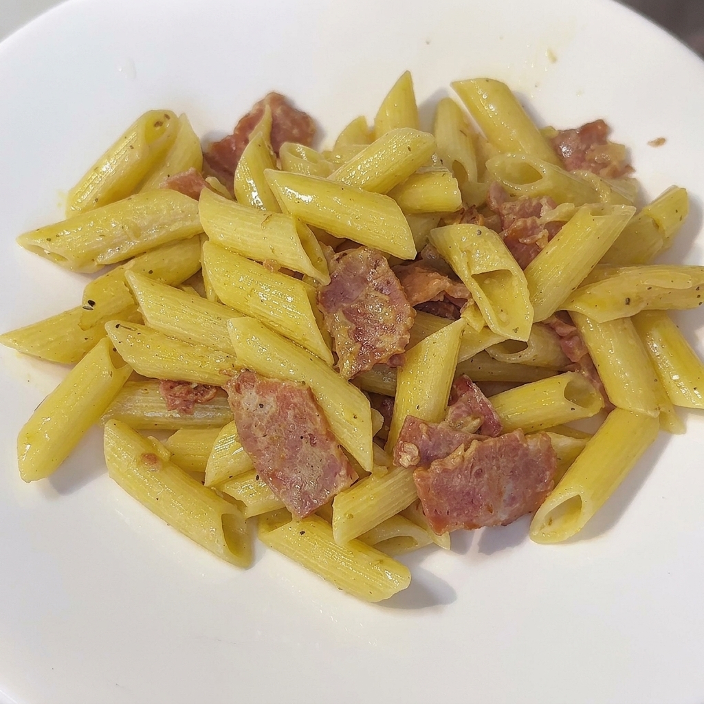 Une poêle de pennes crémeuses remuée avec une spatule.
