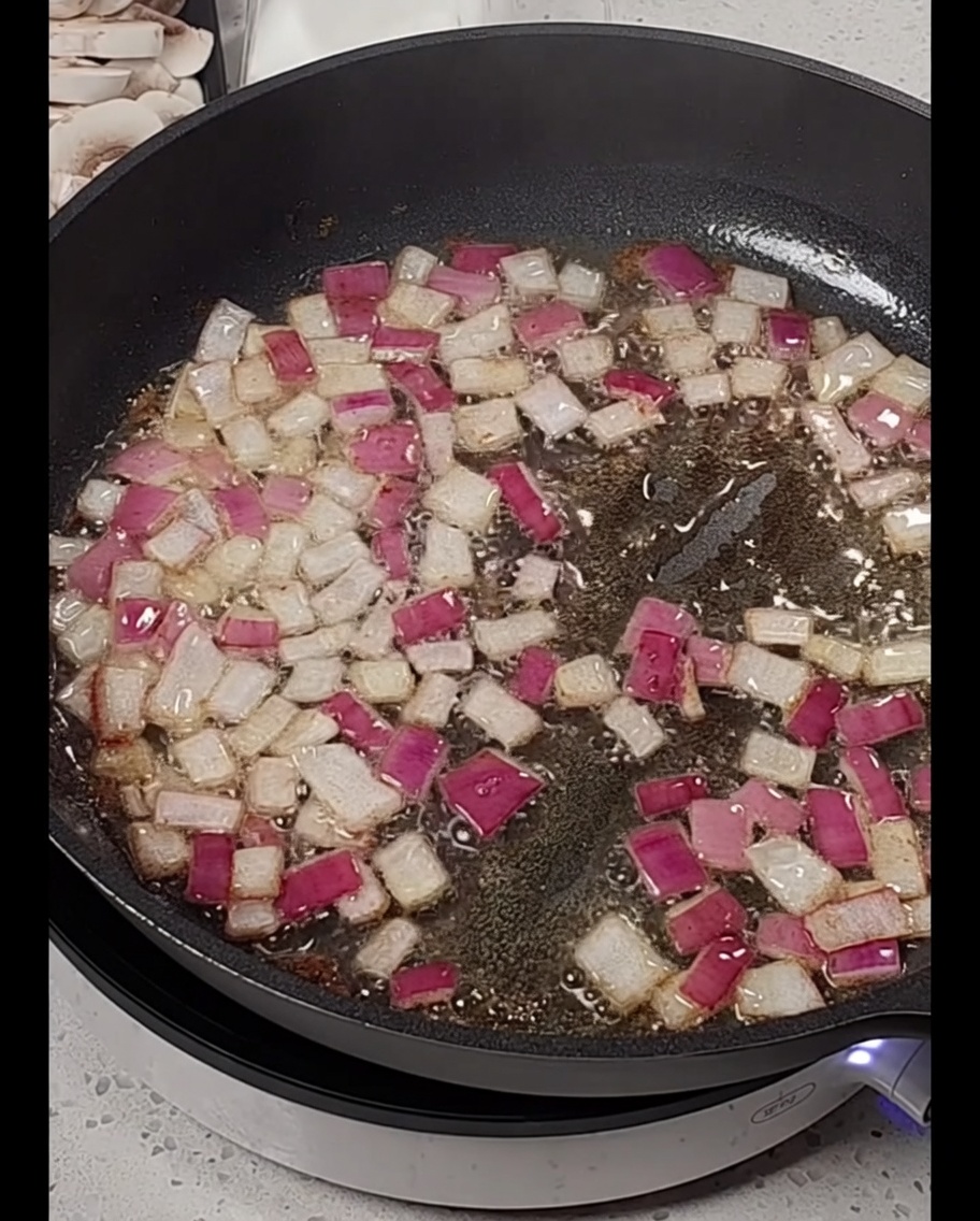 Bâtonnets de lardons ajoutés à une poêle contenant des oignons rouges ramollis.