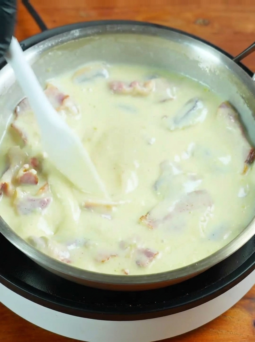 Spaghettis cuits ajoutés dans une sauce blanche frémissante dans une grande poêle.