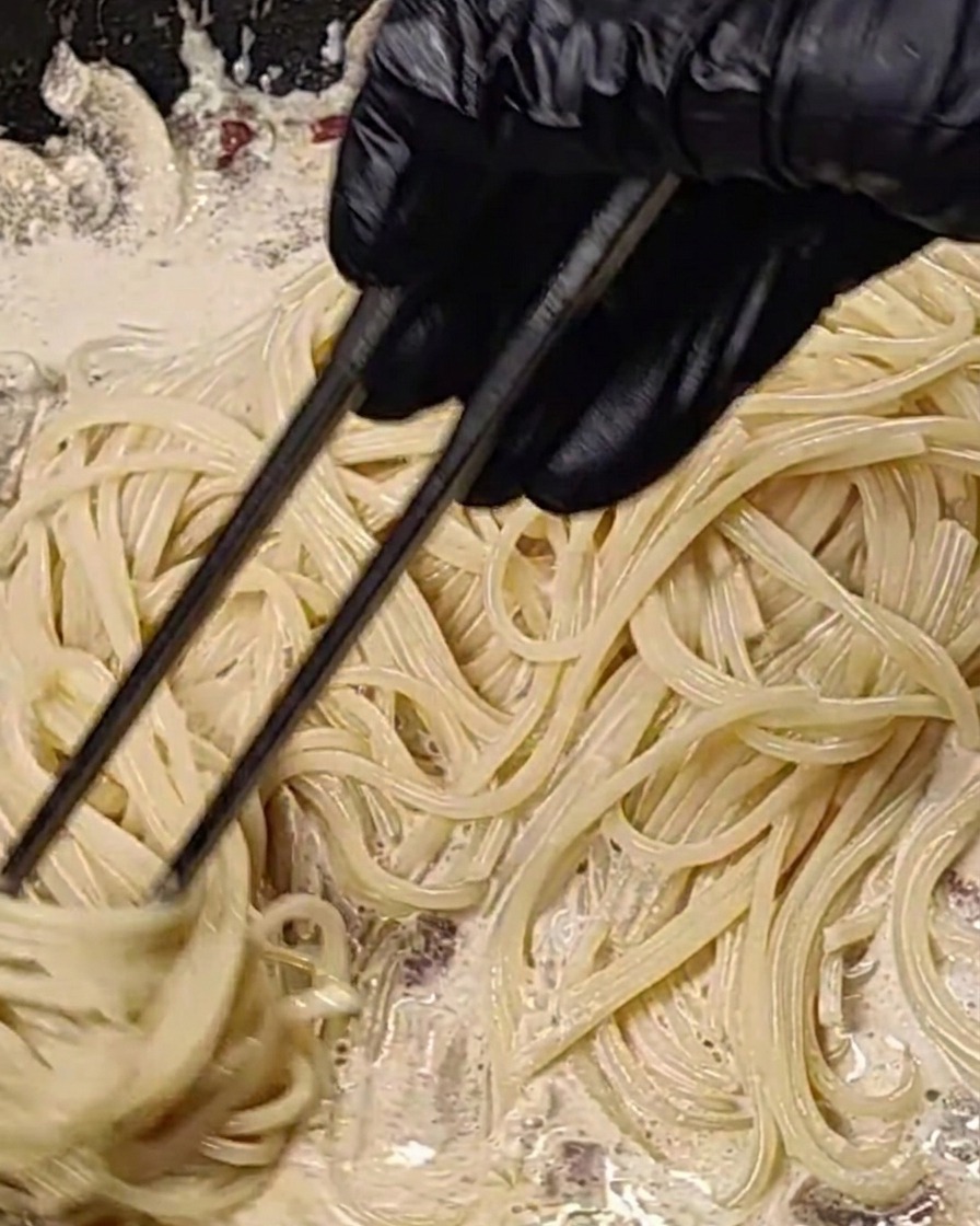 Spaghettis mélangés dans une sauce crémeuse aux lardons et champignons dans une poêle chaude.