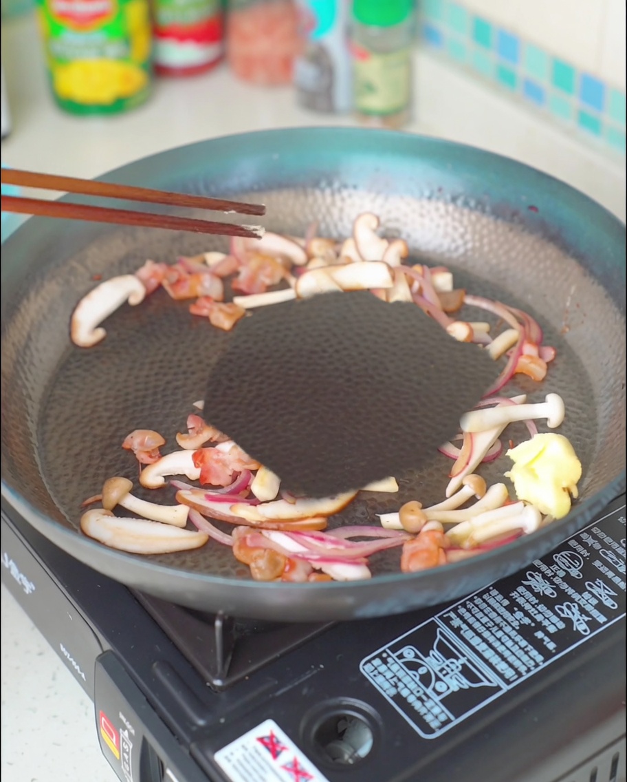 Un morceau de beurre qui fond dans le mélange de bacon, champignons et oignons.