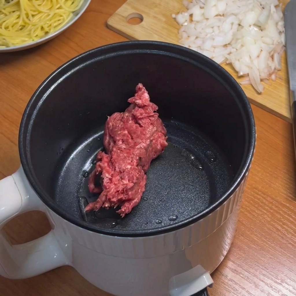 Du bœuf haché qui dore dans une petite casserole électrique à laide dune spatule en silicone bleu clair.