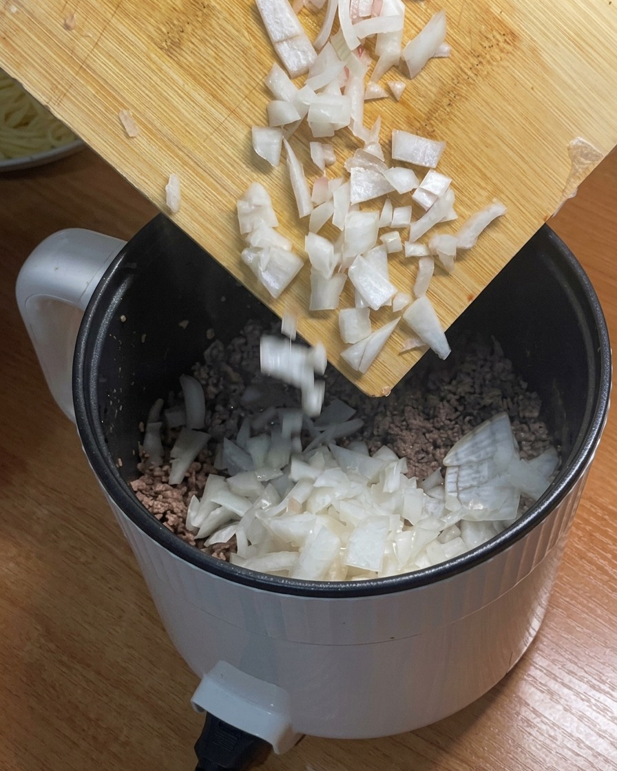 Des oignons blancs émincés ajoutés dans la casserole avec le bœuf haché doré.