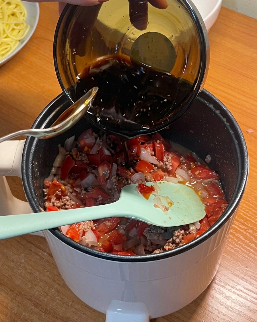 Une sauce dassaisonnement foncée versée dun bol dans la casserole avec les tomates, le bœuf et les oignons.