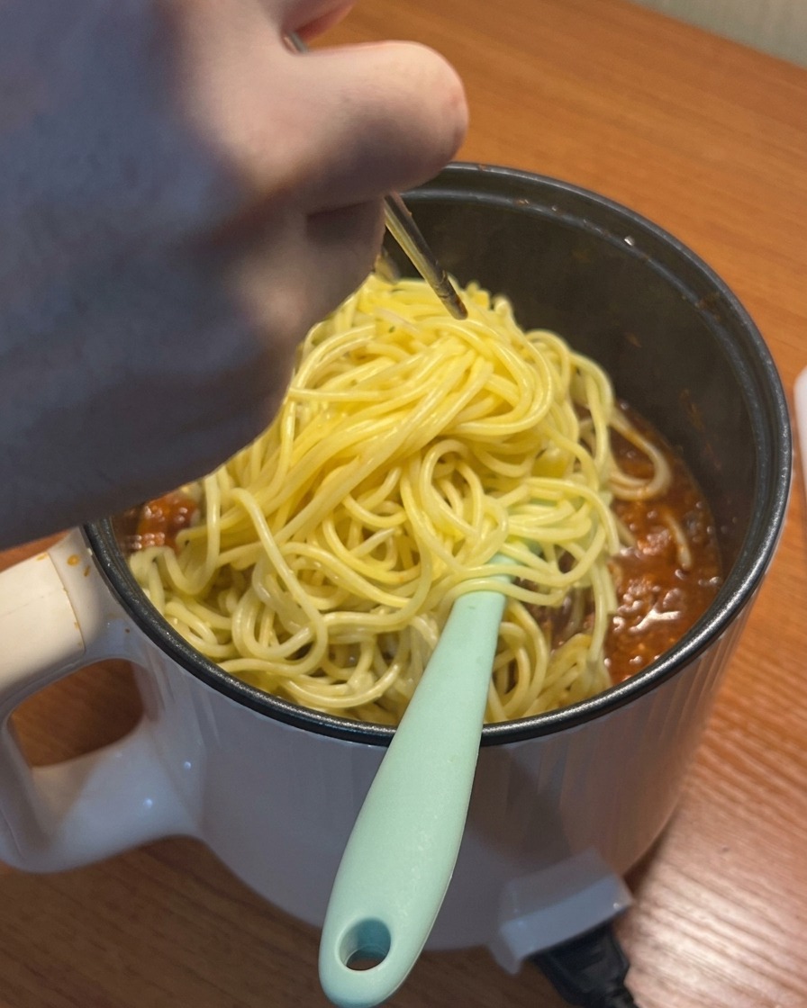 Des spaghettis cuits ajoutés à la sauce tomate à la viande qui mijote.