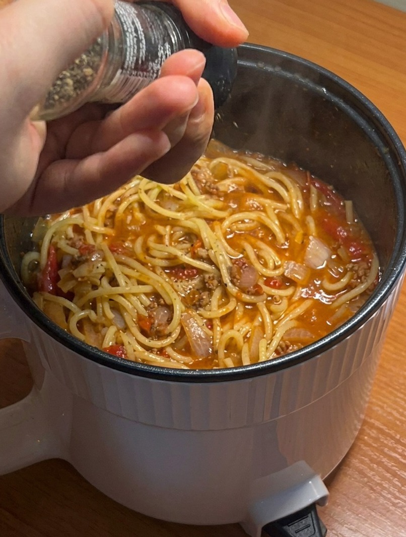 Gros plan sur une casserole de spaghettis à la viande terminés, assaisonnés de poivre noir fraîchement moulu.