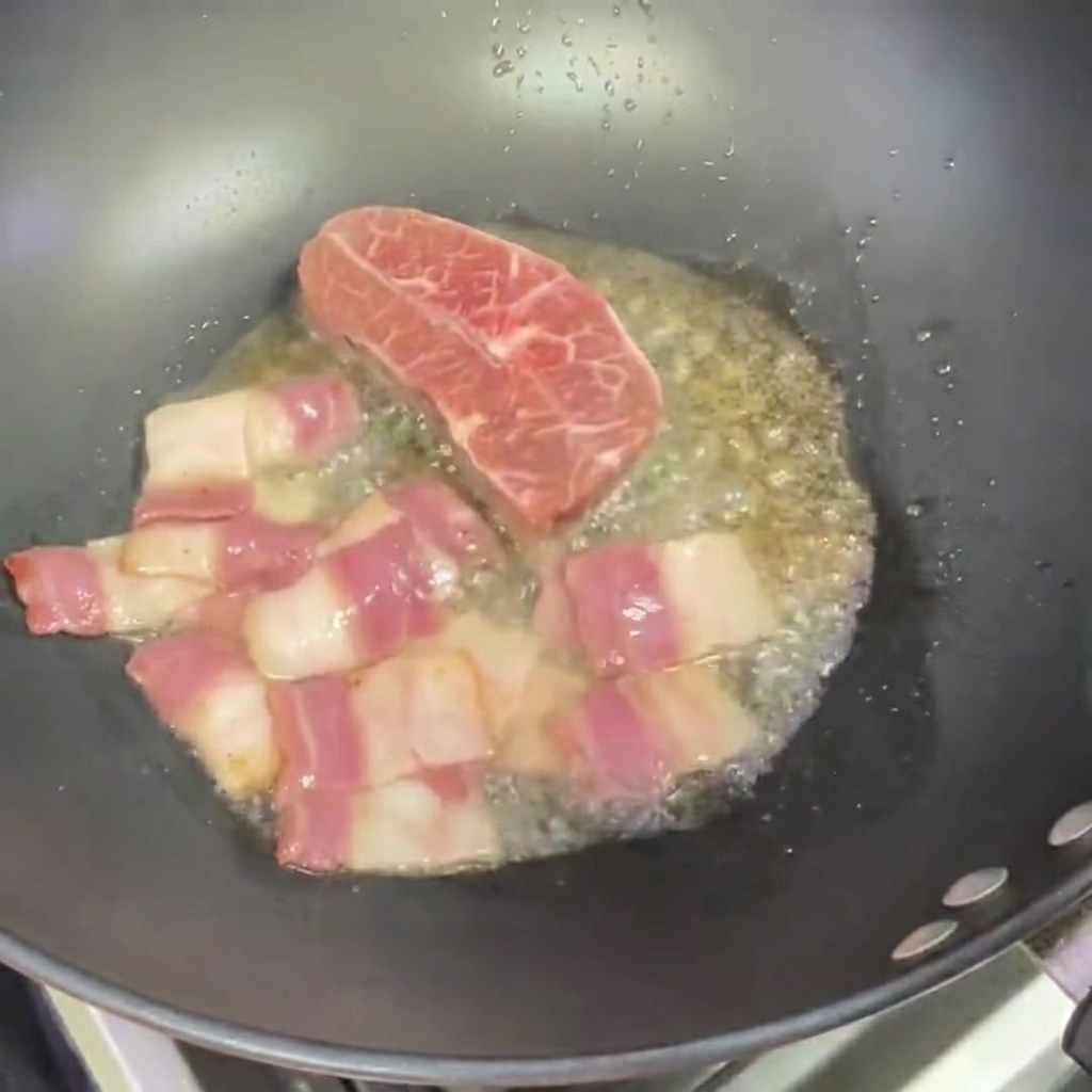 Deux petits steaks en train de frire dans un wok à côté du bacon.