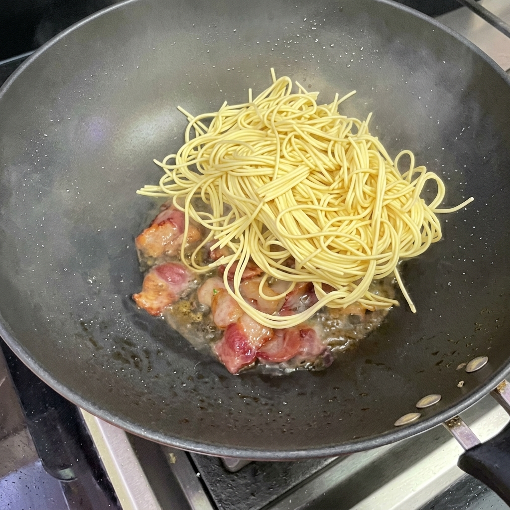 Spaghettis ajoutés dans le wok contenant le bacon.