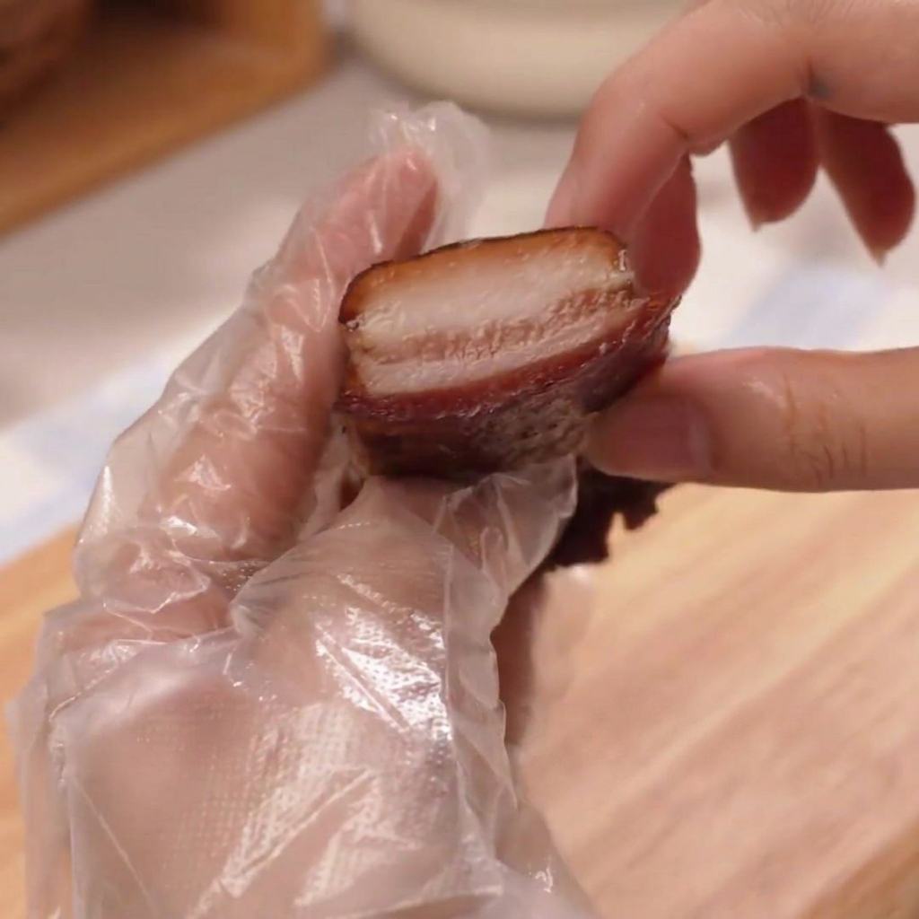 Une main gantée tenant une tranche épaisse et juteuse de jambon rôti.