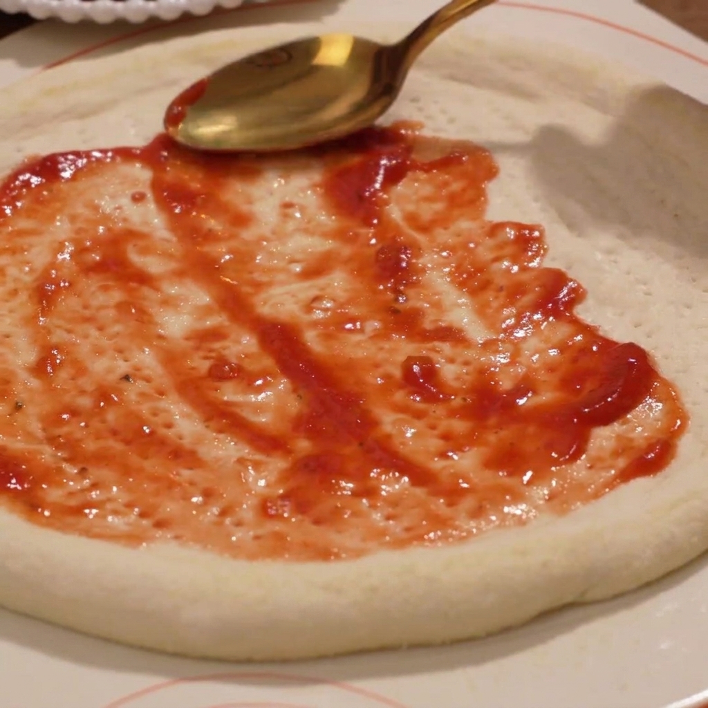 La sauce tomate étant étalée uniformément sur la base de pâte à pizza crue.