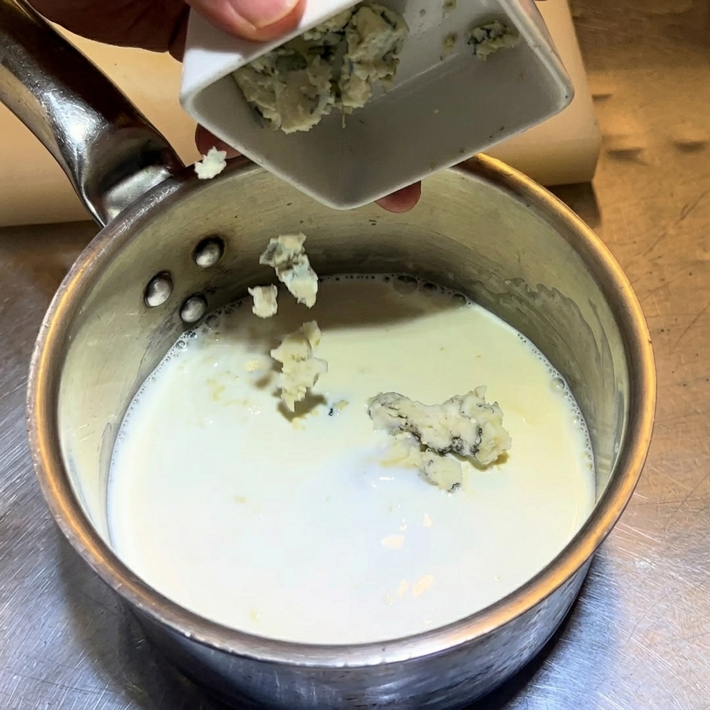 Ajout de morceaux de fromage bleu dans le mélange de lait et crème.