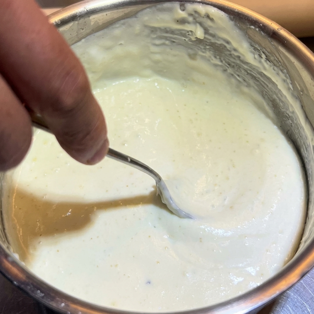 Une cuillère en métal remuant la sauce épaisse et crémeuse dans la casserole.
