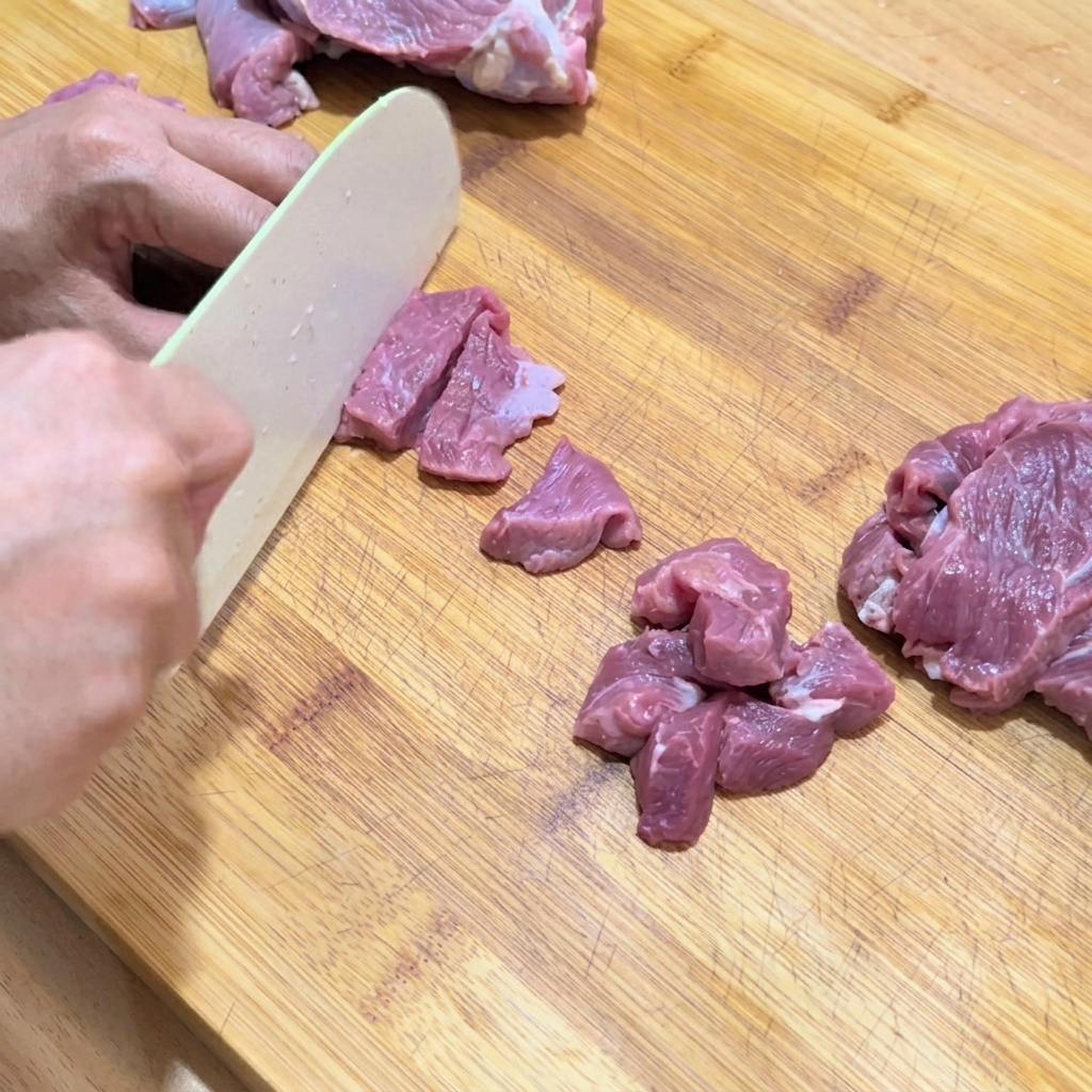 Des mains coupant de la viande de bœuf crue en petits cubes uniformes sur une planche à découper.