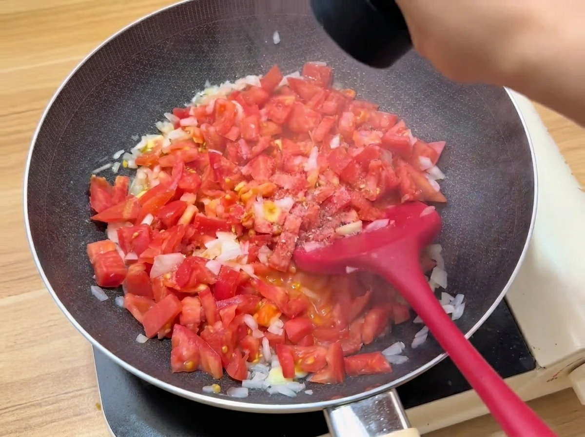 Les dés de tomates cuisant dans une poêle avec lajout des assaisonnements.