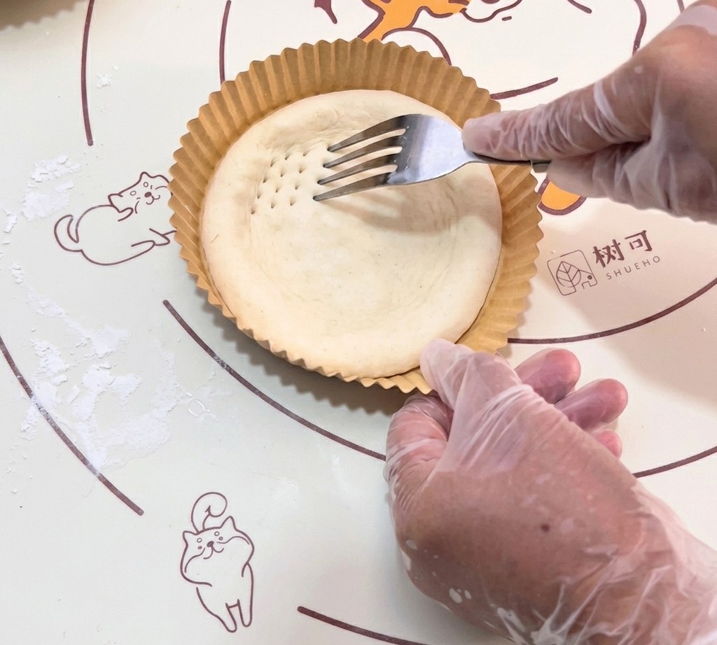 Une fourchette formant de petites perforations sur toute la surface de la pâte crue.