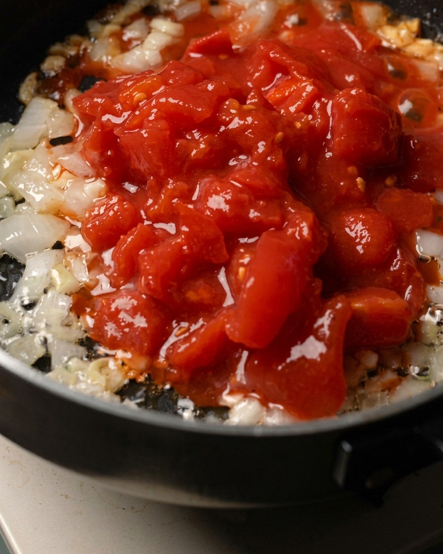 Oignon haché, ail et tomates concassées cuisant dans une poêle.