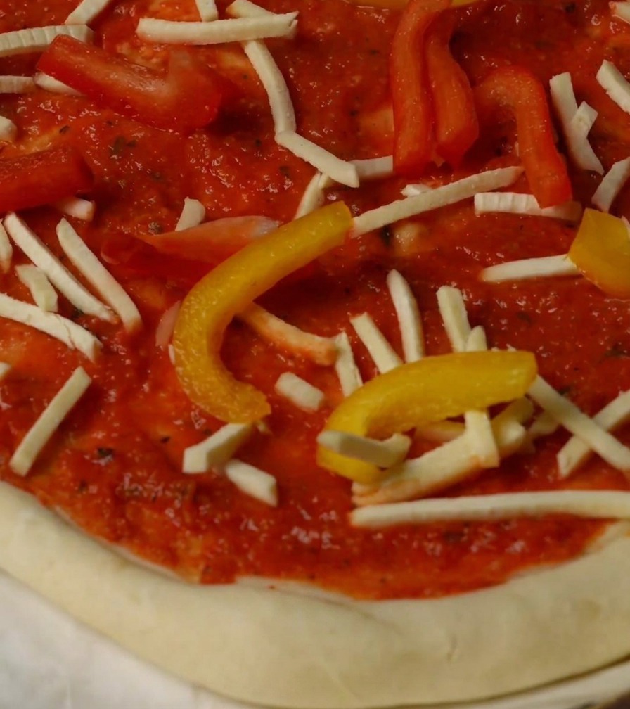 Pizza garnie de poivrons, de fromage et de morceaux de homard, prête à être mise au four.