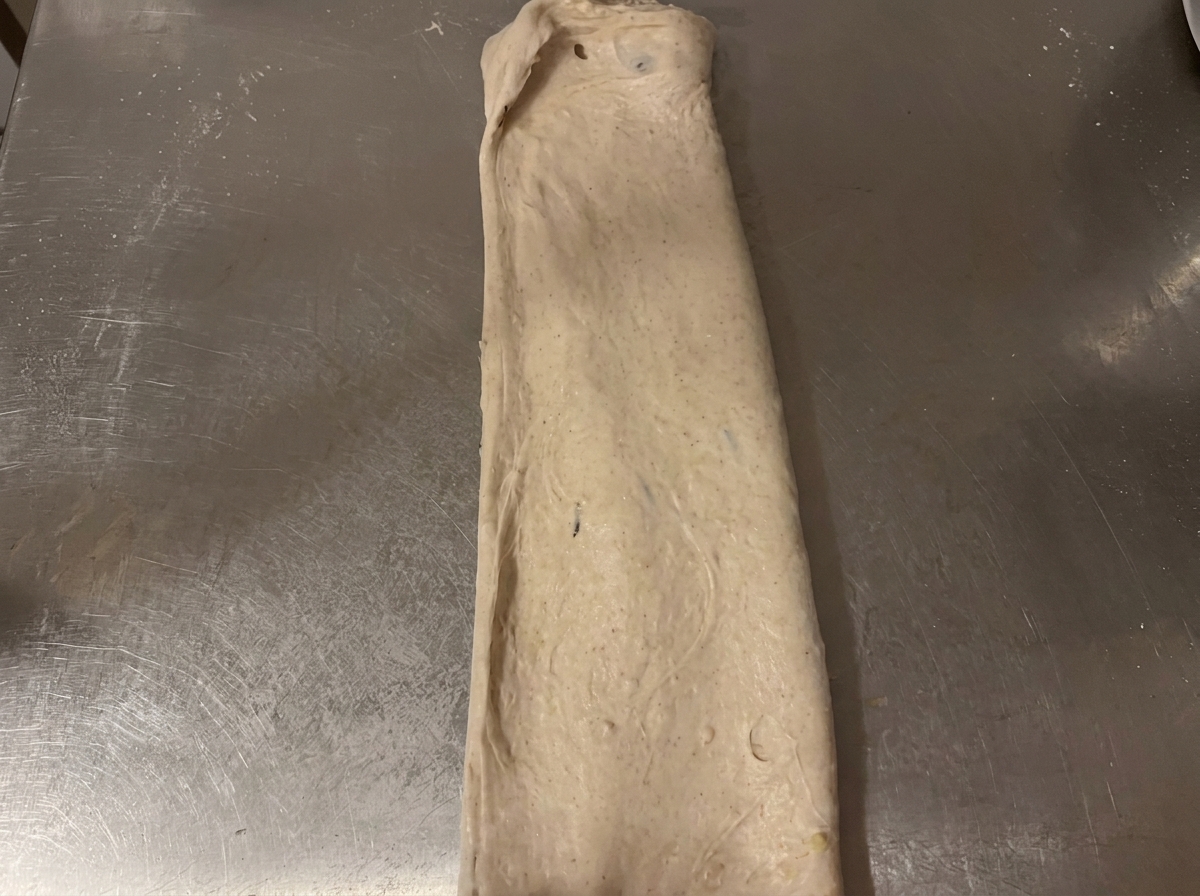 Pâte crue repliée en forme rectangulaire sur un plan de travail en inox.