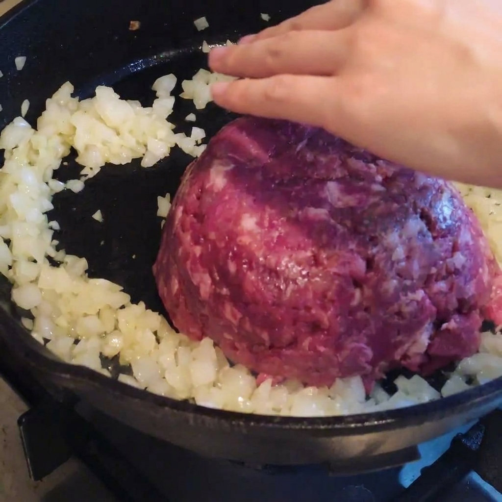 Bœuf haché ajouté aux oignons dans la poêle.