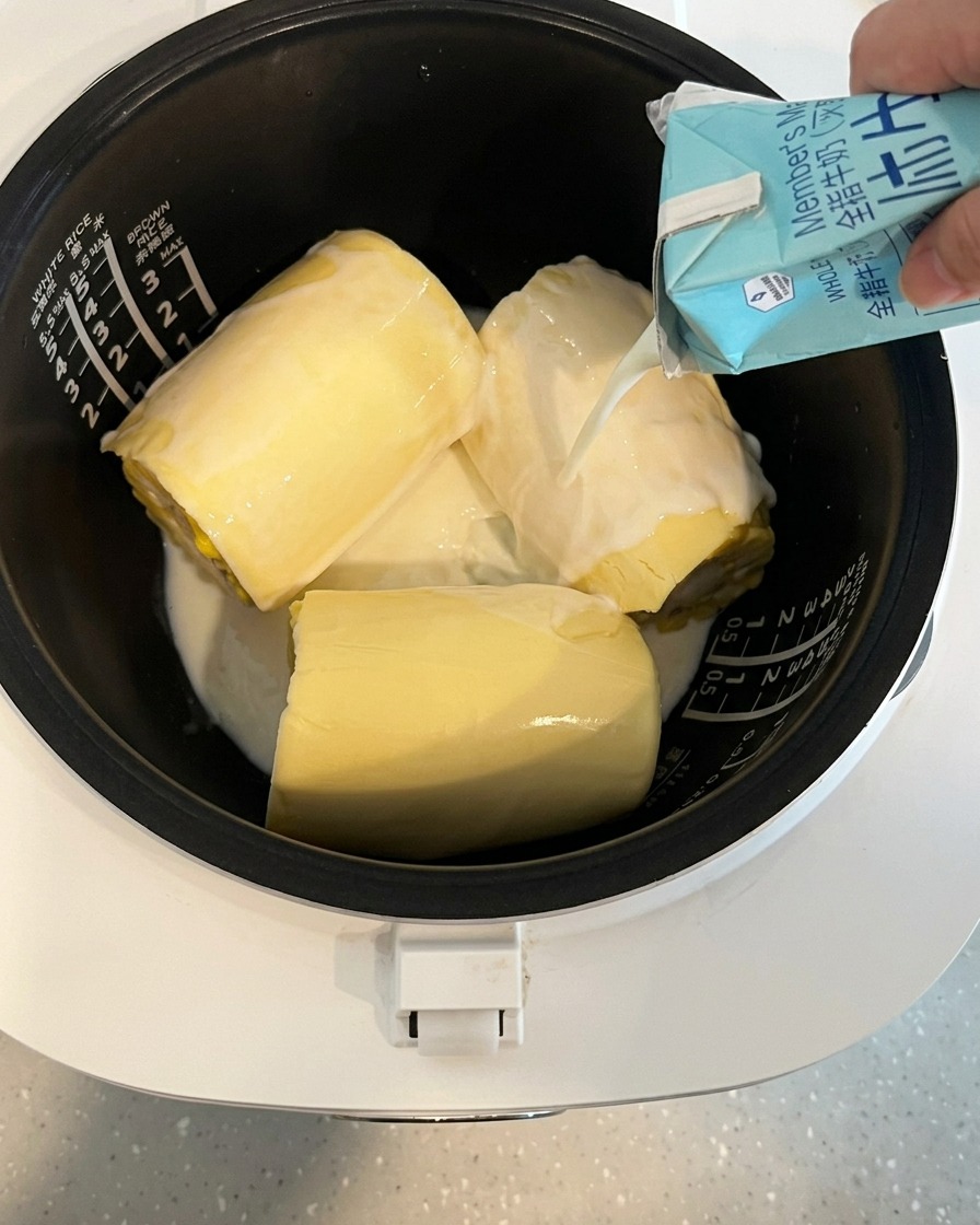Lait versé depuis une brique dans la cuve du cuiseur à riz contenant le maïs et le fromage.