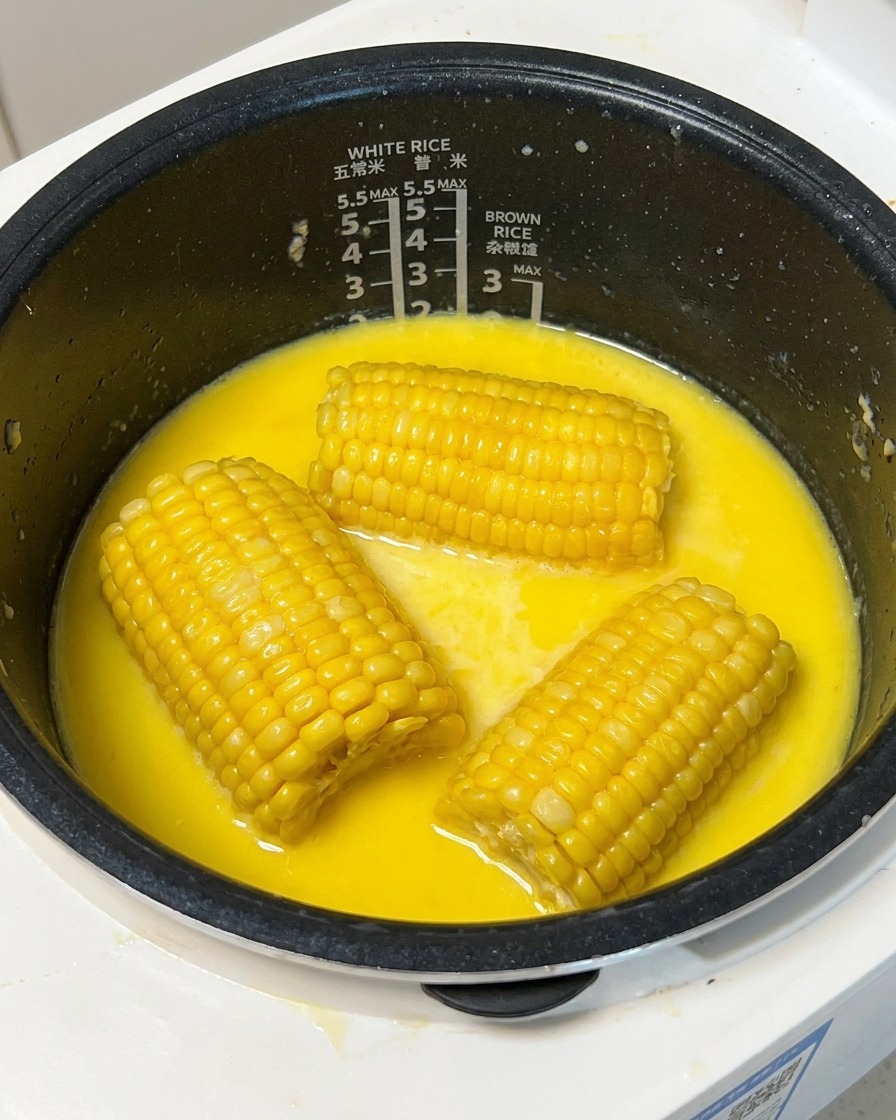 Un morceau de maïs jaune cuit retiré du bouillon laiteux dans le cuiseur à riz à laide dune pique en bois.