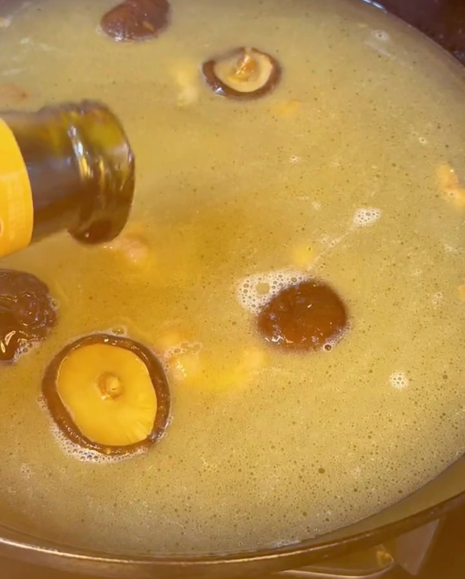 Sauce huître versée dans un bouillon doré bouillonnant rempli de champignons shiitake.