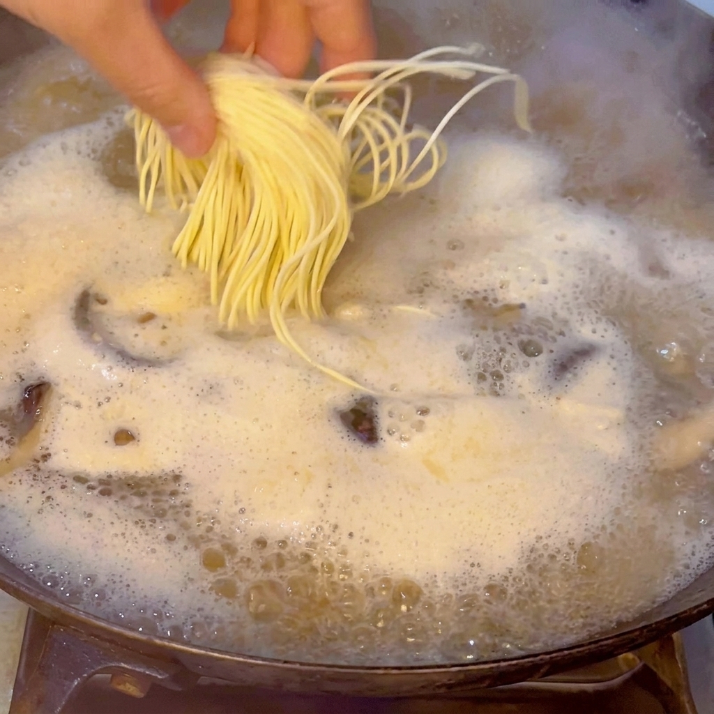 Une main déposant délicatement un paquet de nouilles ramen fraîches dans le bouillon bouillonnant.