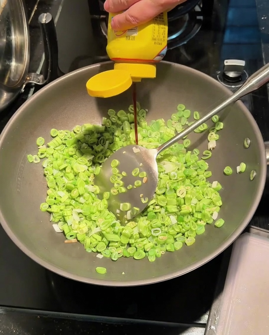 Ajout de sauce dassaisonnement dans le wok avec les haricots et les oignons.