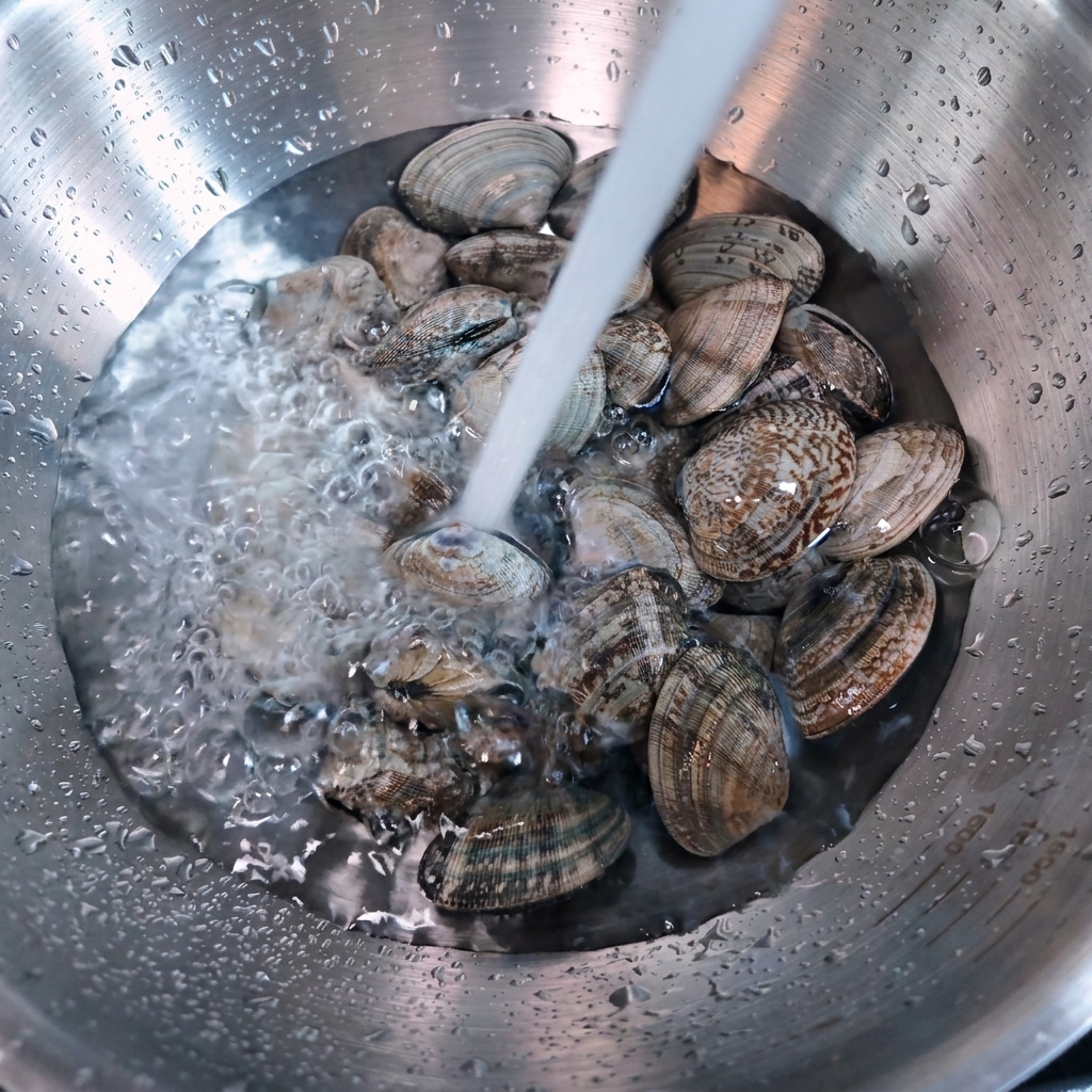 De leau coule sur des palourdes fraîches dans un bol en inox.